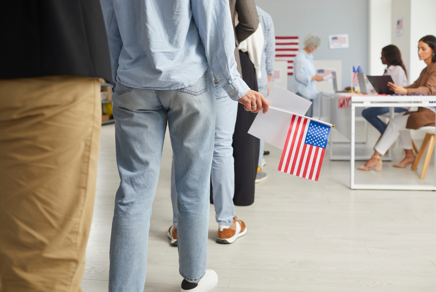 Cropped photo of a group of unrecognizable American citizens people standing in polling station. Voters standing in a queue at vote center getting ballot paper.